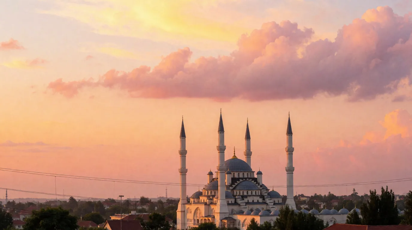 Pembe bulutlu akşam göğünde, dört minareli bir cami silüeti ve çevrede alçak kent yapıları görülüyor