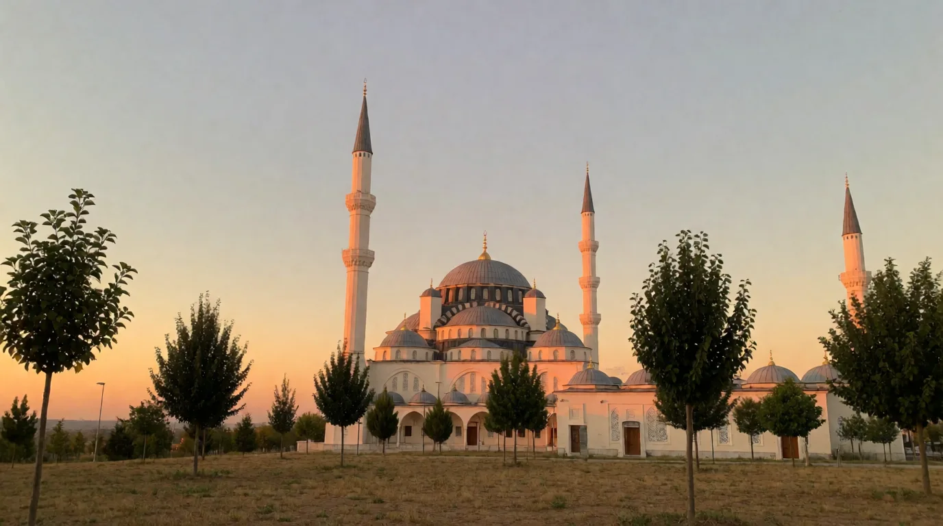 Gün batımında ağaçlarla çevrili bir alanda yükselen kubbeli cami ve ince minareler